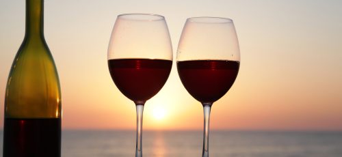 Bottle of wine with wine glasses at sunset on the sea background